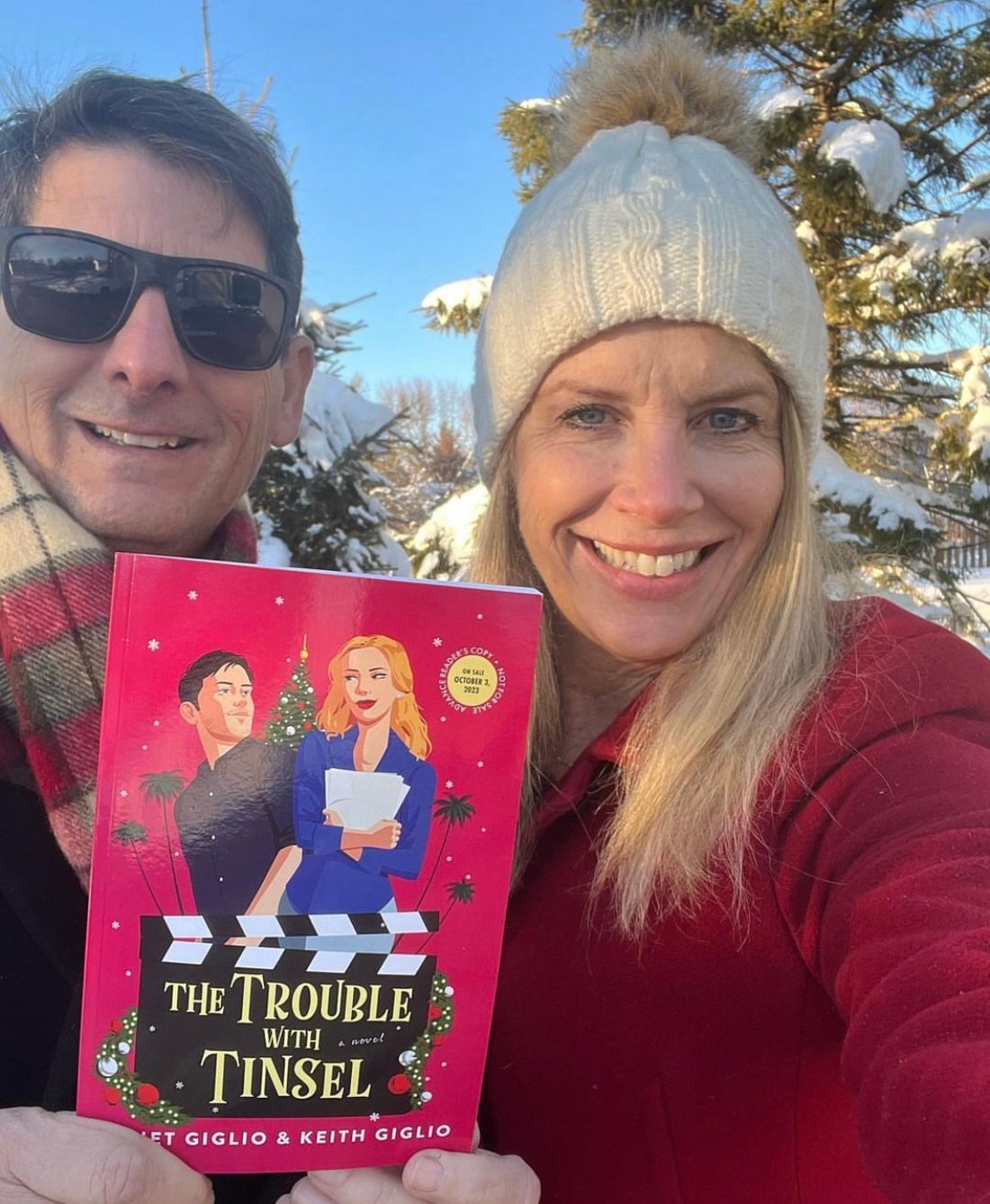 Juliet and Keith Giglio in the snow holding their novel The Trouble with Tinsel