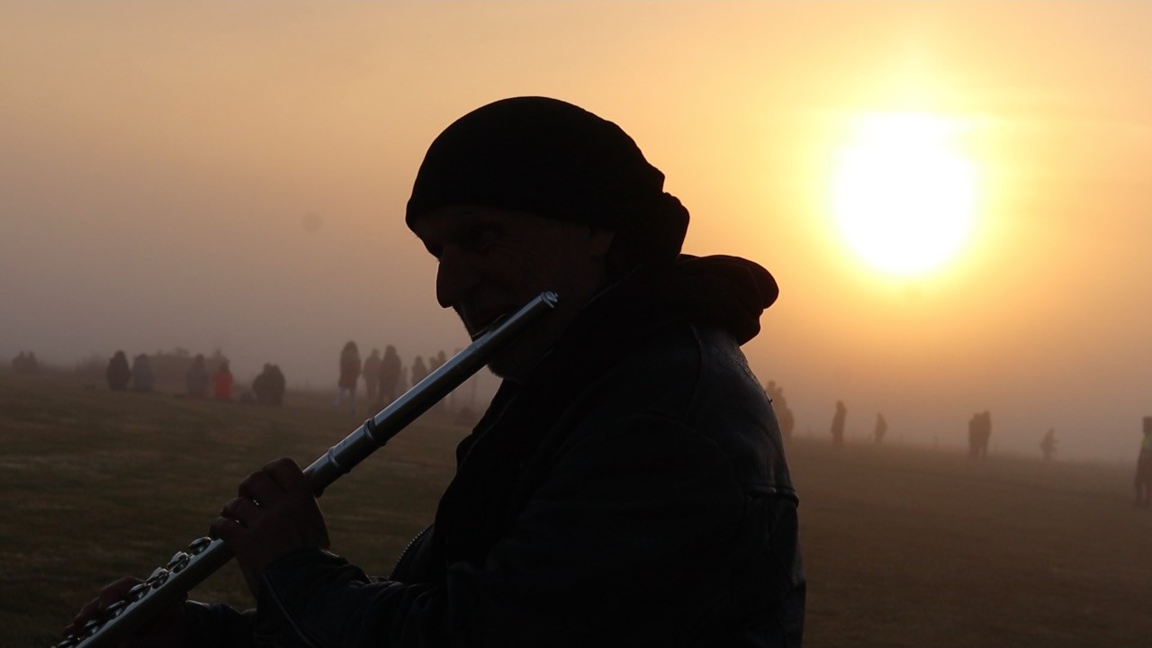 David Heath playing flute in silhouette against a misty sunrise