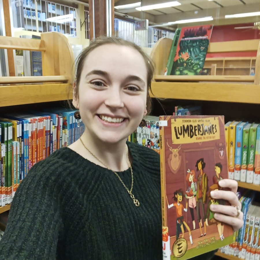 Emily Rundle holding a copy of Lumberjanes in the library