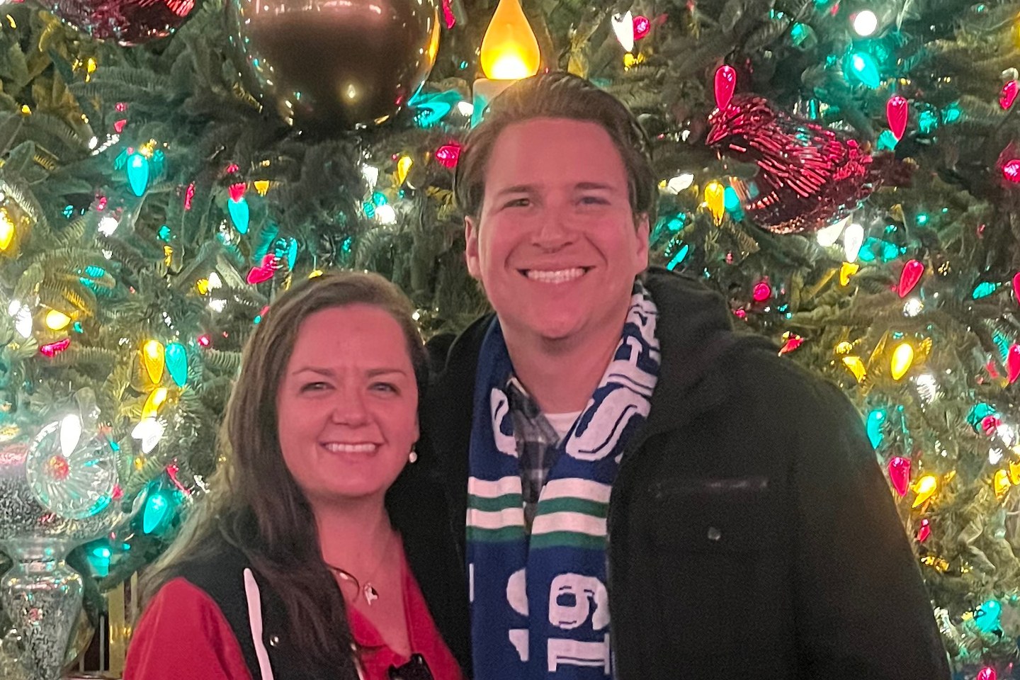 Kaylah and Anthony Cantu smiling in front of a Christmas tree strung with coloured lights