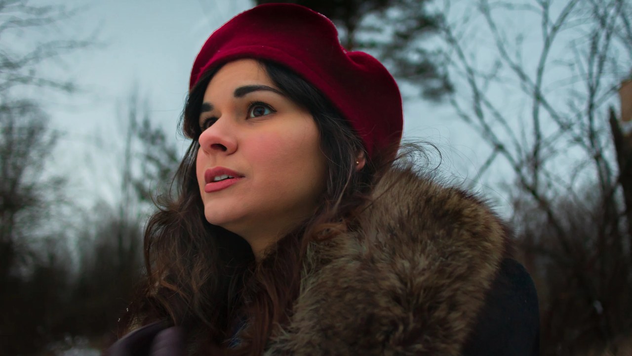A woman in a red beret looking up in a winter forest